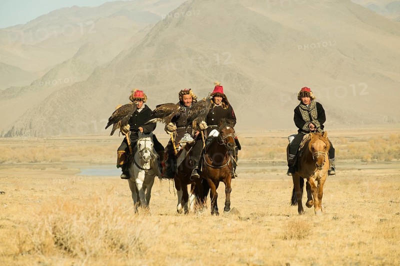 Four Kazakh eagle hunters on their horses on the way to the Eagle Festival in Sagsai