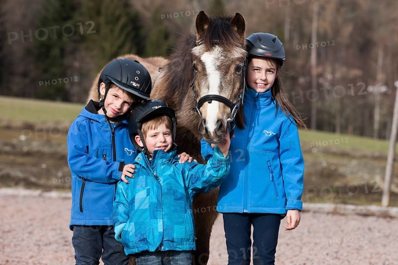Three children wearing riding helmets standing beside a pony
