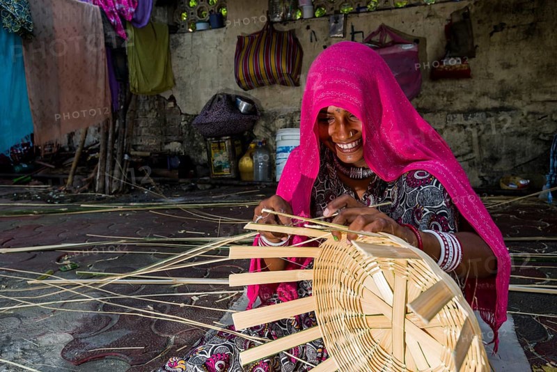 Woman covered in a pink veil is braiding a basket on the pavement