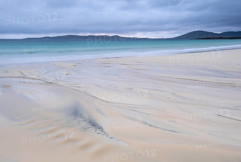 Water flows into the sea at low tide via a sandy beach