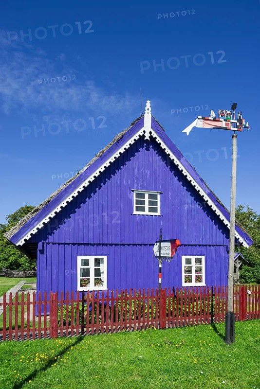 Curonian flag in front of a traditional wooden house