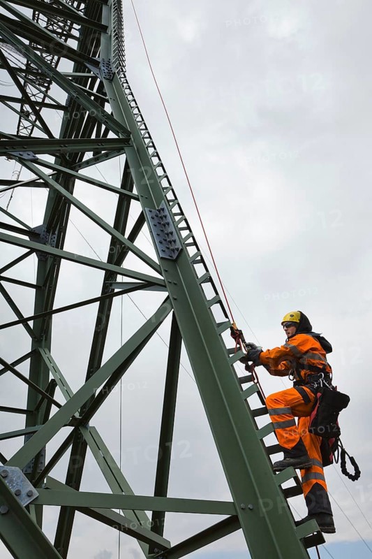 Overhead transmission cable installer climbing a mast to install insulated cable on a newly built high-voltage transmission mast