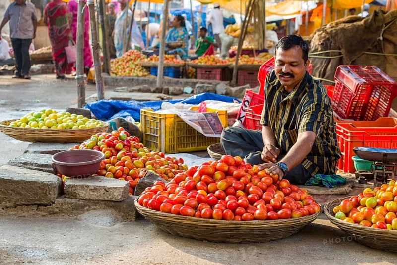 A man is selling tomatoes at the weekly vegetable market