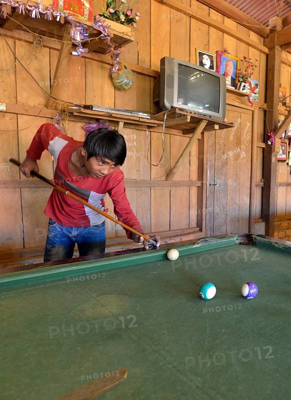 Cambodian youth playing pool billiards in a simple wooden hut