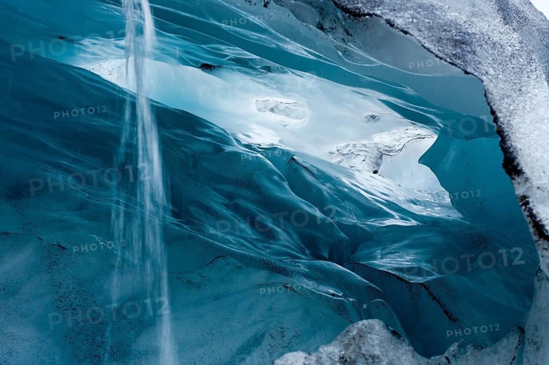 View into a blue-green ice cave with condensation water draining off