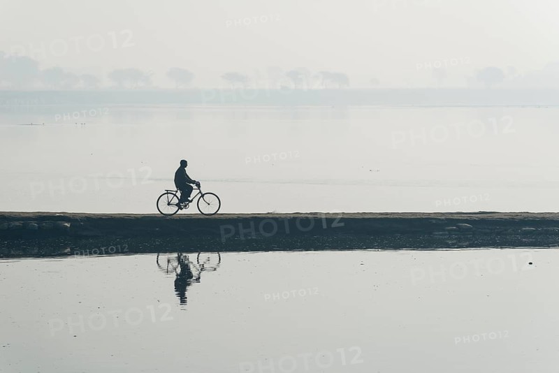 A cyclist crossing the Yamuna river on a dam in the morning haze