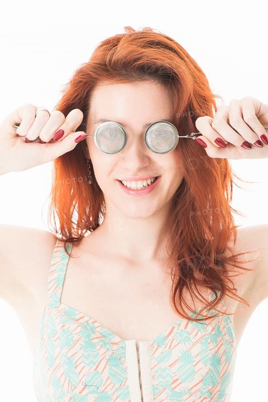 Young red-haired woman holding tea infusers in front of her eyes