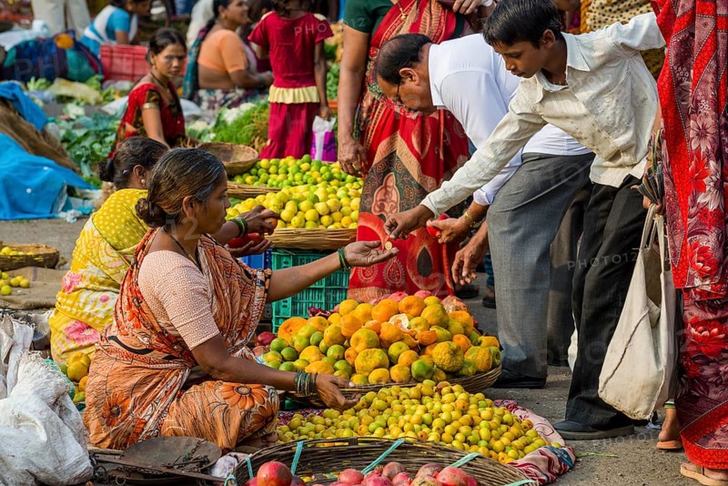 A woman is selling oranges and other fruits at the weekly vegetable market