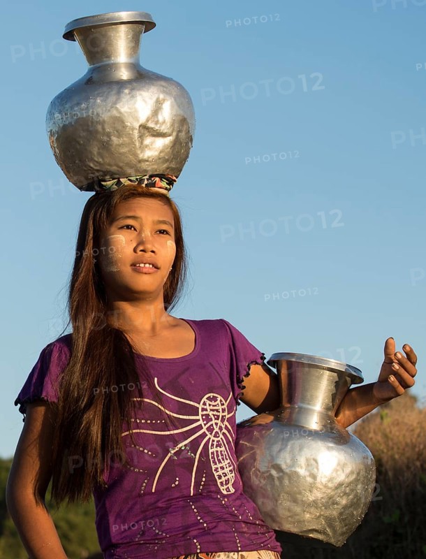 Girl with tanaka in her face carries water vessels made of aluminum