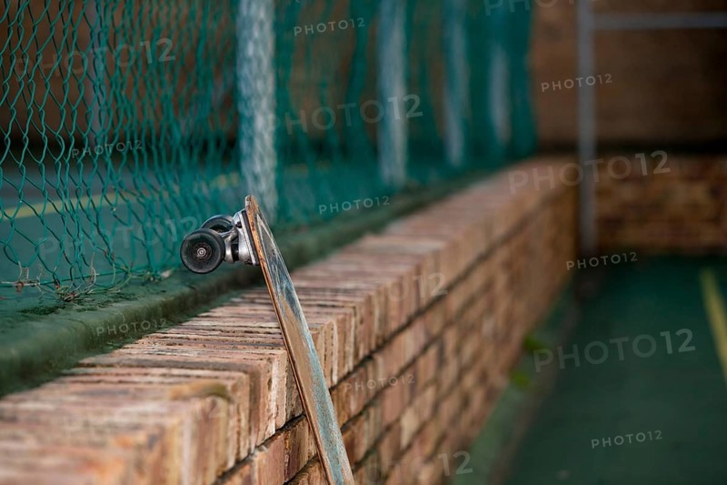 Skateboard leaning against a brick wall in tennis court yard