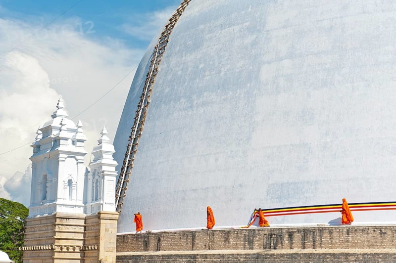 Monks tying a cloth around a large white stupa