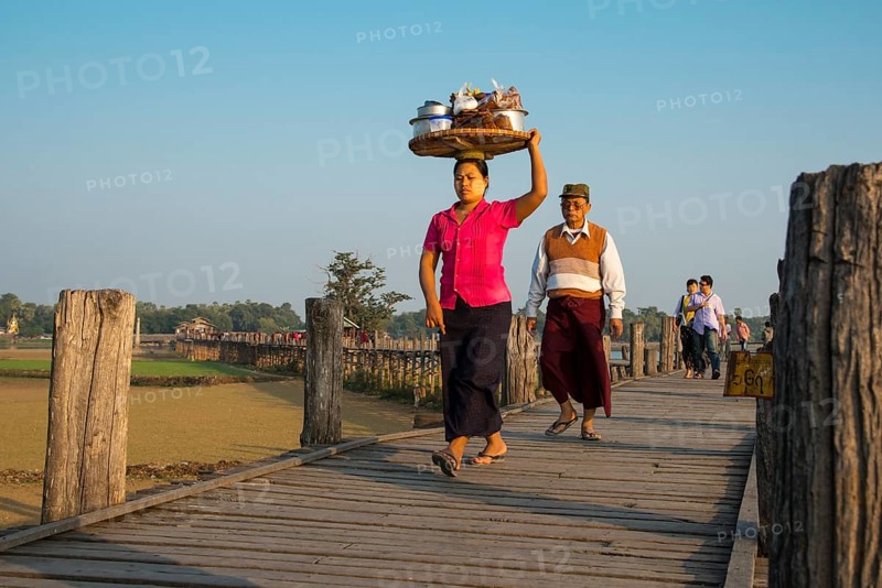 Woman with tanaka on her face carrying food on her head on a teak bridge