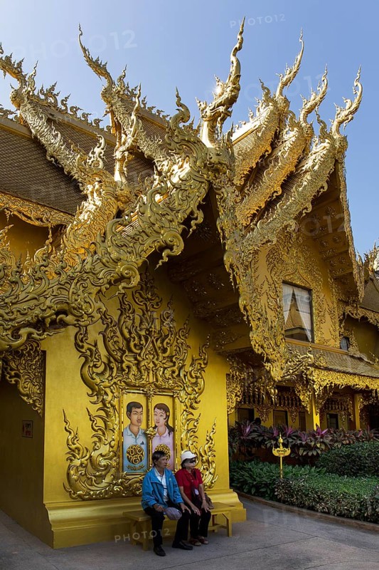 Tourists sitting in front of the gilded toilet house at Wat Rong Khun