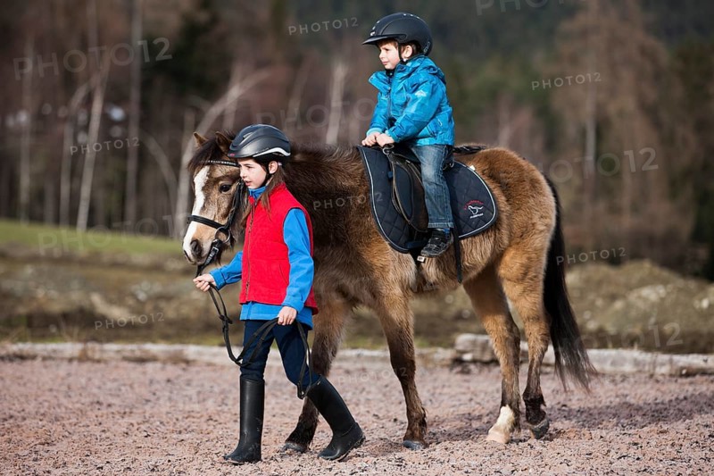 Girl leading a pony with a young child riding it