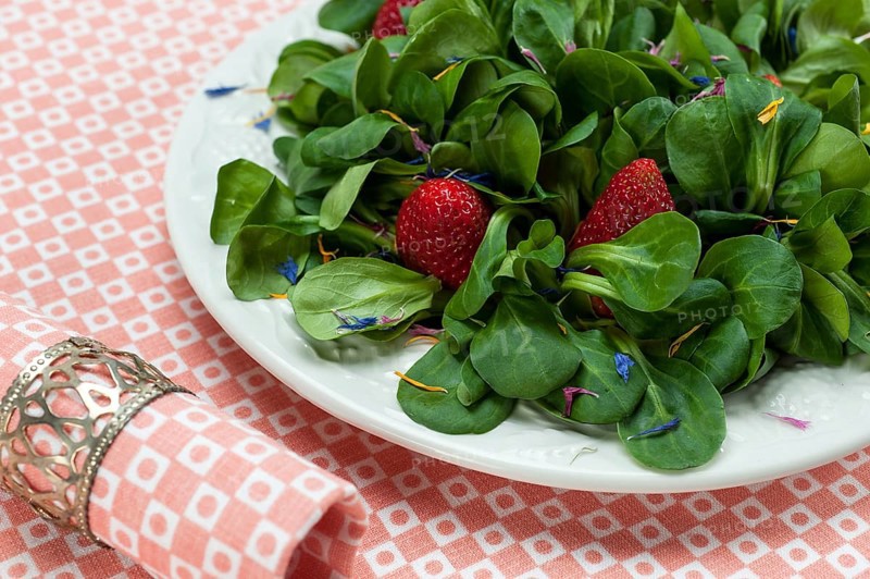 Lamb's lettuce with strawberries and flower petals served on a plate