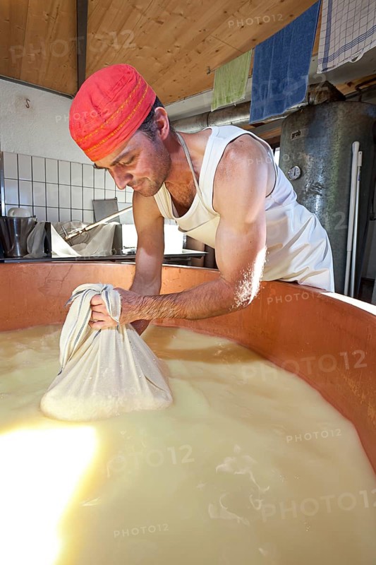 Dairyman drawing cottage cheese with a cloth from the copper kettle for a first test