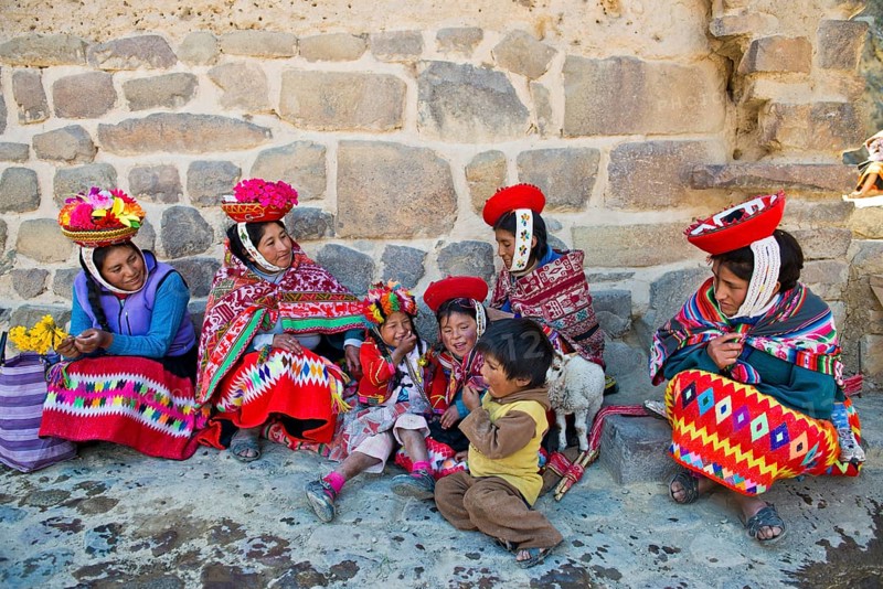 Women and children in traditional dress of the Quechua Indians sitting on the floor in front of a wall