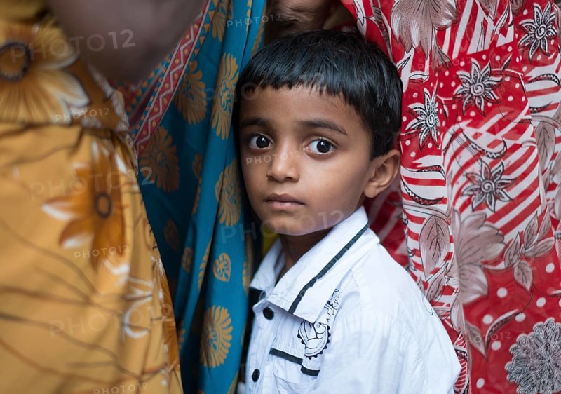 Shy Indian boy hiding between women