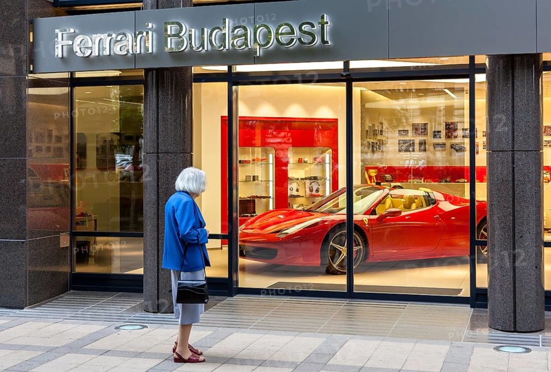 Elderly woman standing in front of the shop window of a Ferrari dealer