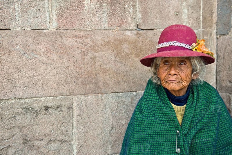 Portrait of an elderly woman in traditional dress of the Quechua Indians sitting on the floor in front of an Inca wall