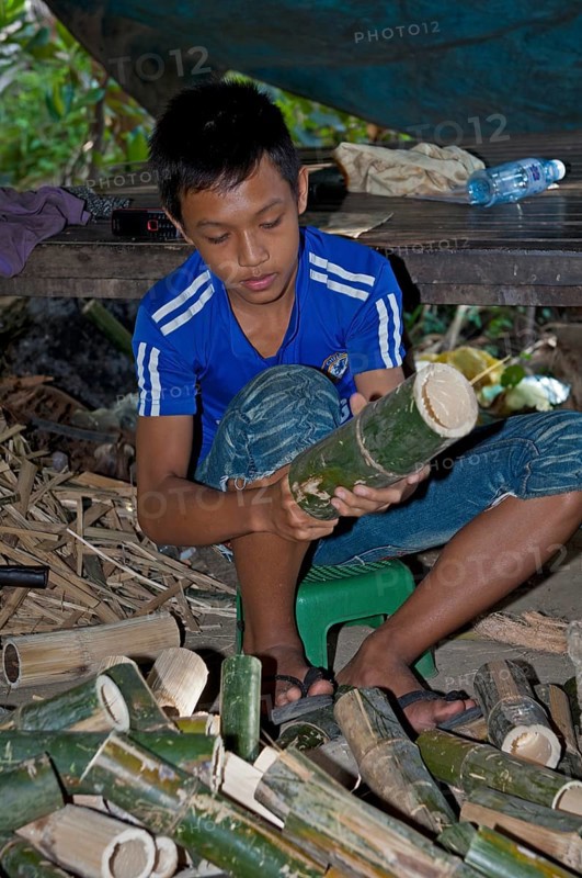 Boy cleaning bamboo tubes used in the preparation of the traditional rice dish Kralan or Khao Lam