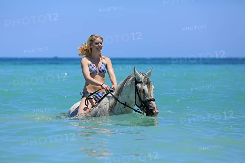 Woman wearing a bikini riding a Barb horse in the sea