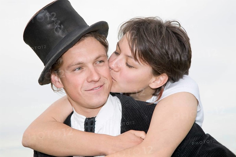 Young man wearing a top hat being tenderly kissed by his partner as he carries her piggyback