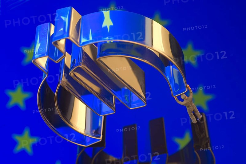 Miniature figure of a worker is carrying the Euro-symbol