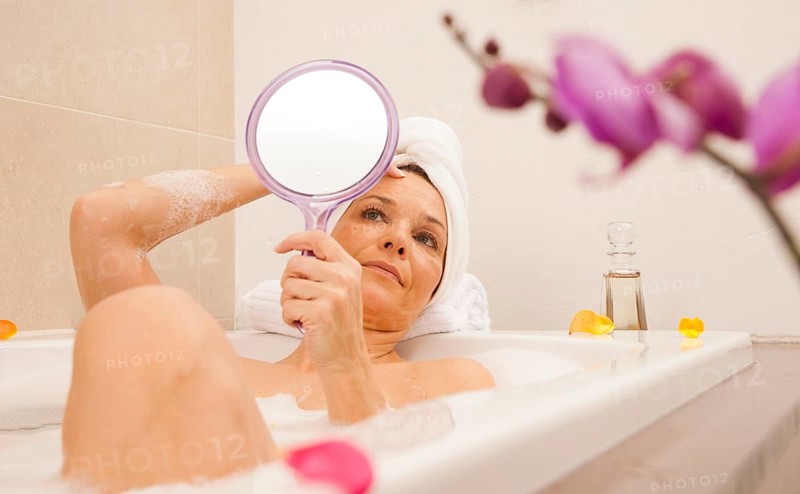 Woman taking a bath and looking at her face with a mirror
