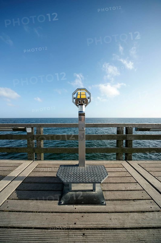 Coin-operated binoculars on a pier in front of the blue sea and blue sky