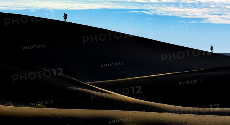 Silhouettes of people climbing a dune