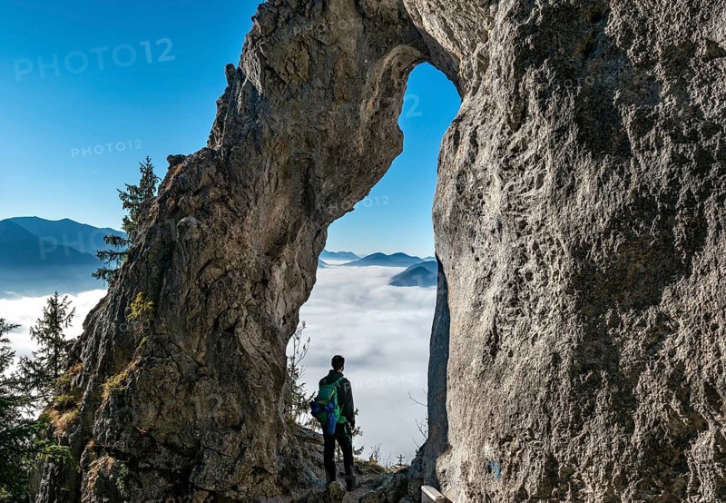 Young man stands in the rock gate Breitensteinfensterl with a view of the high fog above the valley