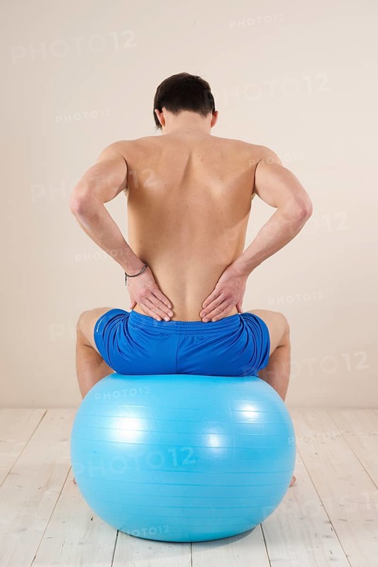 Young man sitting on a gym ball and touching his aching back