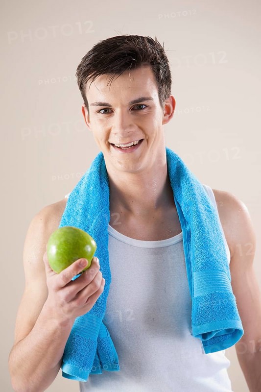 Smiling young man after doing sport holding an apple in his hand