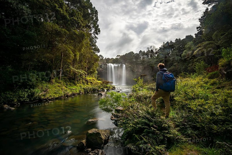 Young man standing in front of waterfall