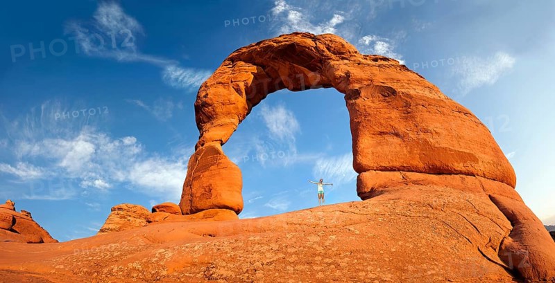 Woman standing under Delicate Arch natural stone arch