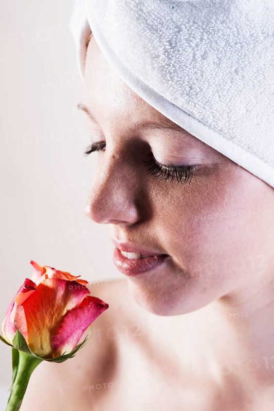 Portrait of a smiling young woman smelling a rose with a towel wrapped around her head