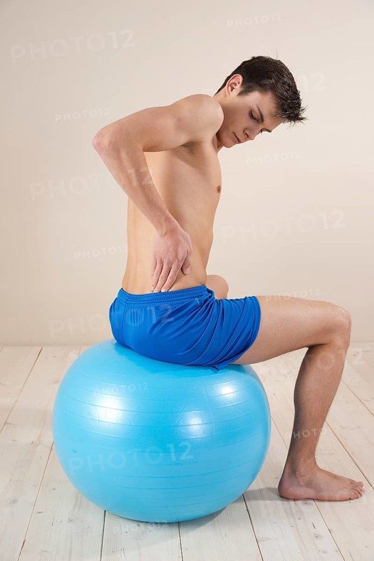 Young man sitting on a gym ball and touching his aching back