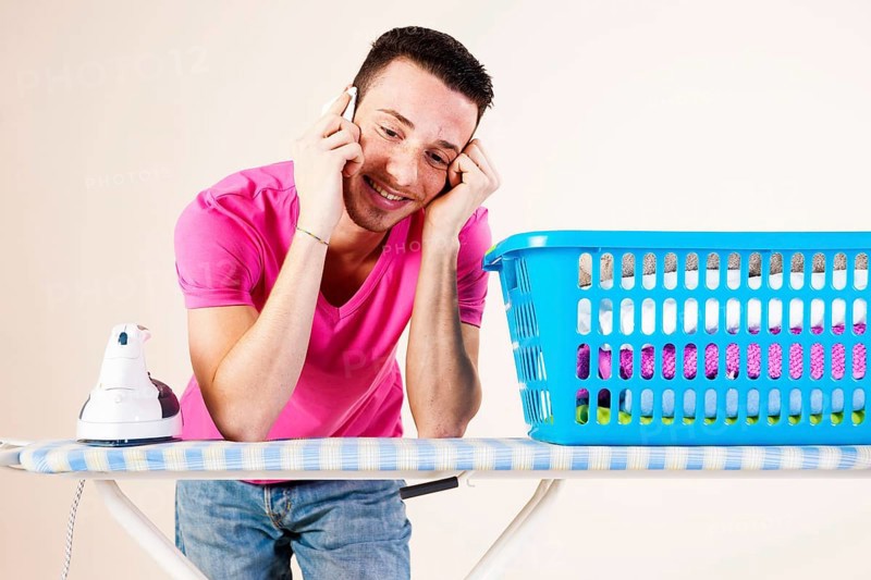 Young man talking on the telephone while leaning on an ironing board