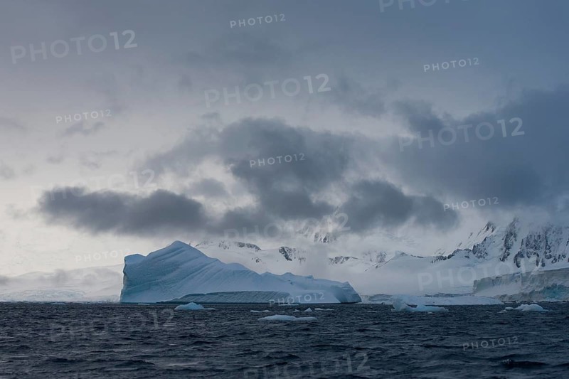 Iceberg in a fjord with mountain scenery and a cloudy sky