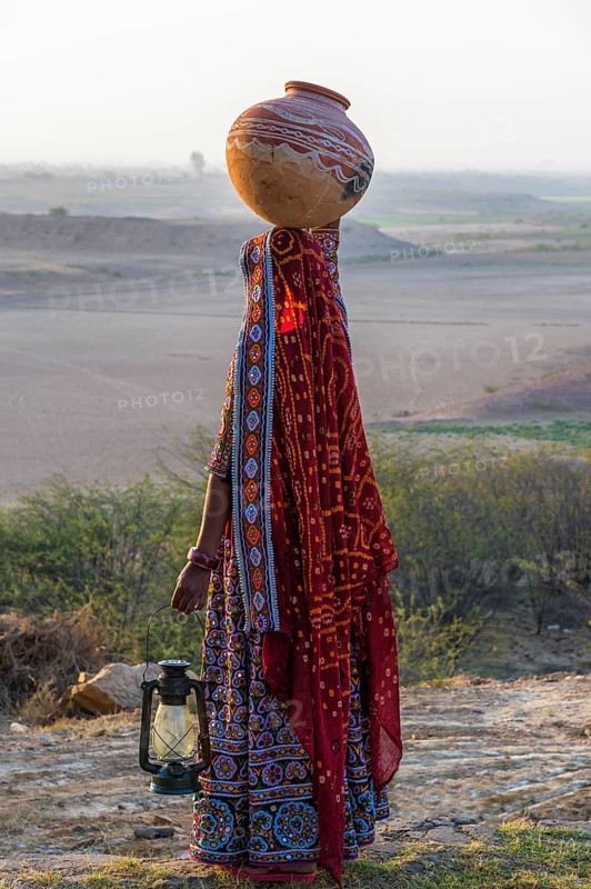 Ahir woman in traditional colorful clothes carrying water in a clay jug on her head