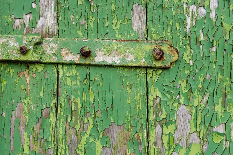Peeling green paint on wooden boards and a hinge