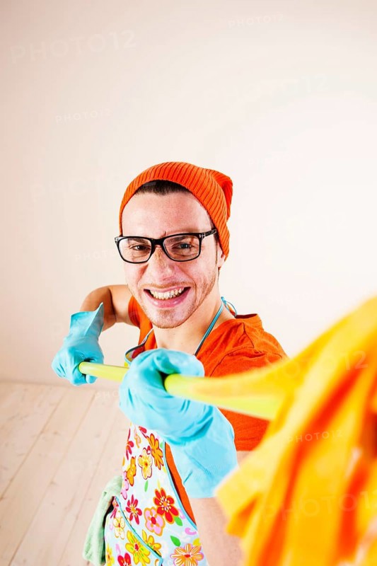 Young man wearing an apron and cleaning gloves holding a cleaning mop