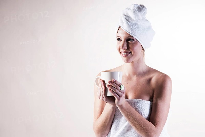 Smiling young woman with a towel wrapped around her head holding a teacup