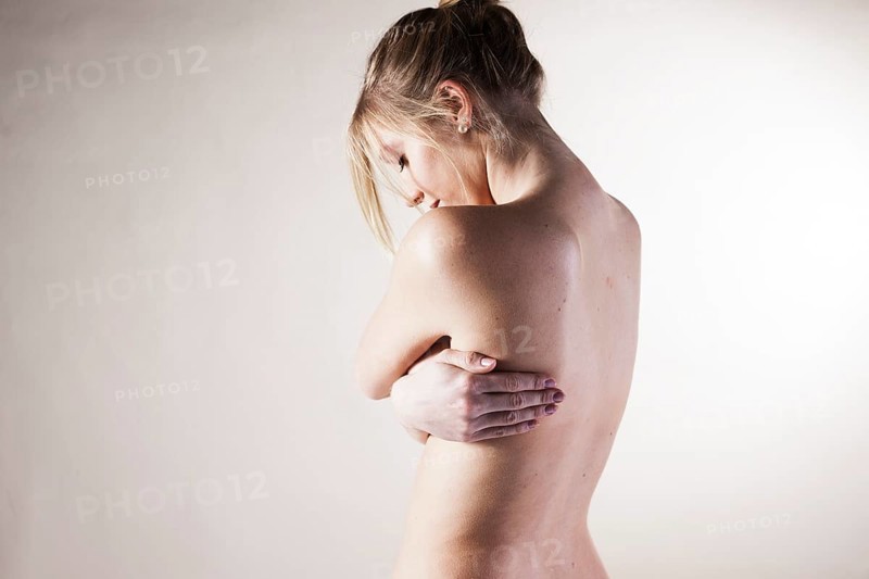 Naked young woman standing with her arms folded