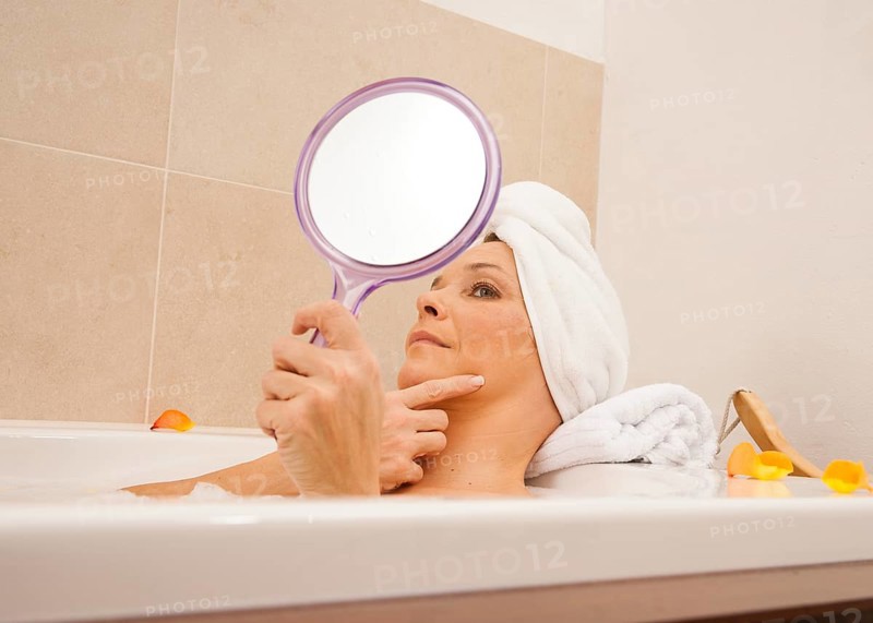 Woman taking a bath and looking at her face with a mirror