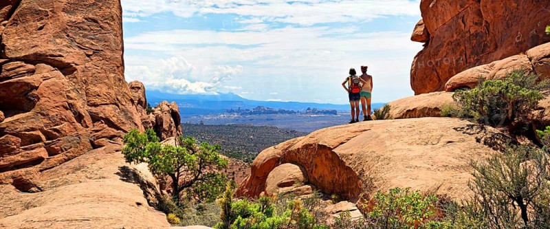 Hikers looking towards the La Sal Mountains from between red sandstone cliffs