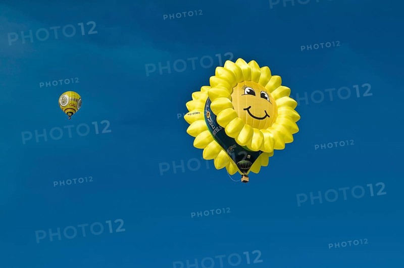 Hot air balloon in the shape of a 'laughing' sun or sunflower against a blue sky