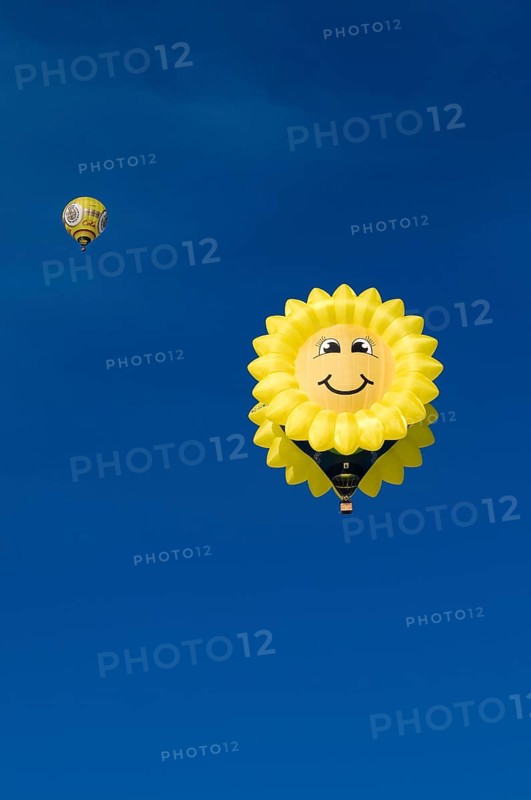 Hot air balloon in the shape of a 'laughing' sun or sunflower against a blue sky