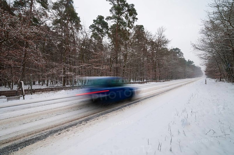 Snow-covered road in winter with car passing by quickly